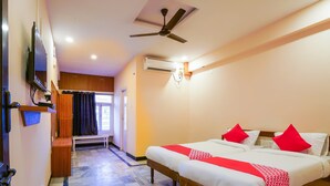 A hotel room with a bed, a ceiling fan, an air conditioning unit, a television, a bench, and a window with curtains. - OYO 49253 Raja Residency (Hyderabad)