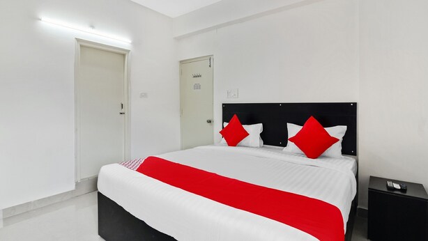 Una habitación de hotel moderna con una cama grande, paredes blancas y una mesita de noche negra con un control remoto.