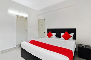 Una habitación de hotel moderna con una cama grande, paredes blancas y una mesita de noche negra con un control remoto.