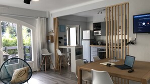 Una cocina moderna con refrigerador, microondas y estufa. Hay un comedor con una mesa de madera y sillas, y una computadora portátil sobre la mesa.