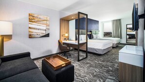 A hotel room with a large bed, a desk, a chair, a sofa, a TV, and a painting on the wall. - SpringHill Suites by Marriott Phoenix Goodyear (Goodyear)