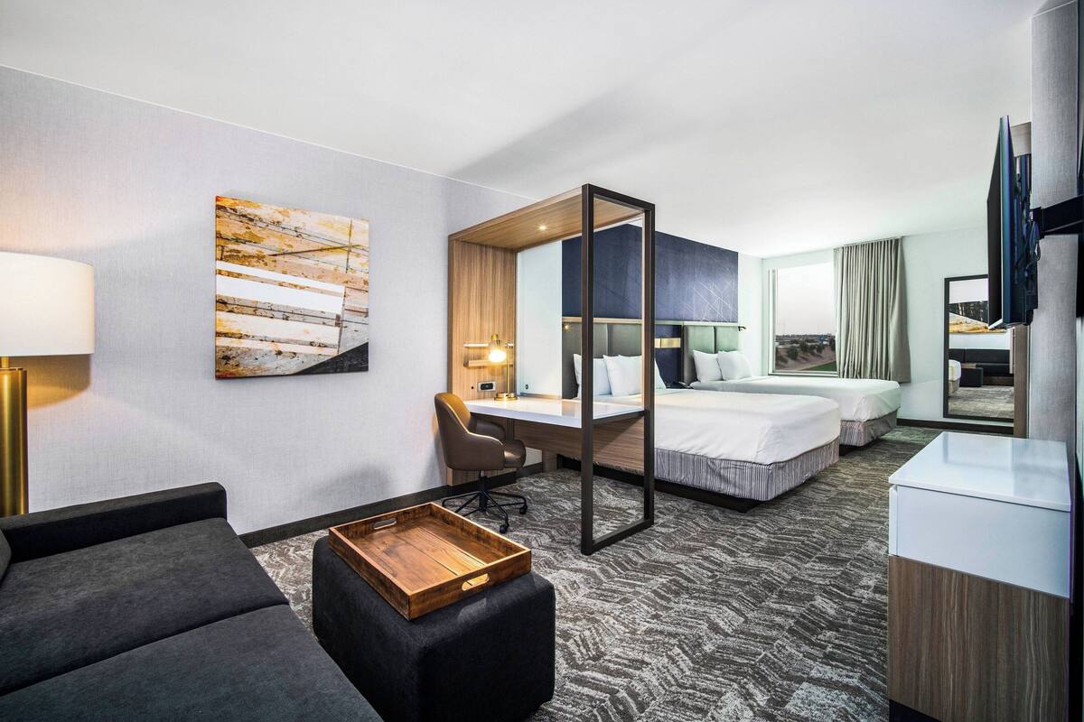 A hotel room with a large bed, a desk, a chair, a sofa, a TV, and a painting on the wall.