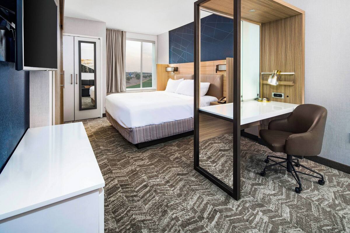 A hotel room with a bed, a desk, a chair, and a large window offering a view.