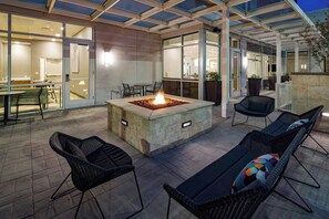 Une terrasse extérieure dotée d’un foyer, de chaises en osier et d’un espace repas fermé par des parois de verre.