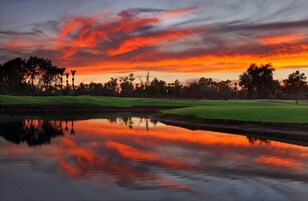 Un campo de golf con un estanque tranquilo que refleja el cielo al atardecer.