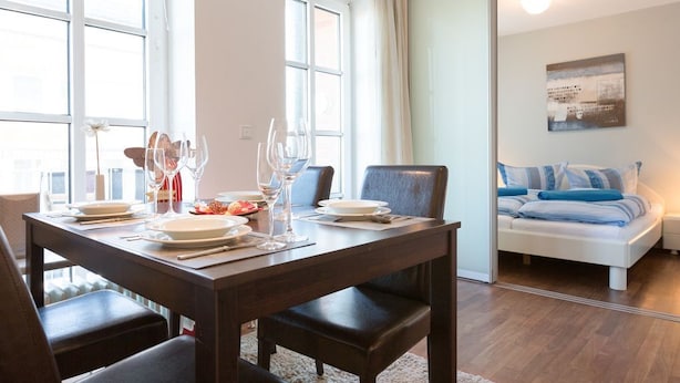 A dining area with a wooden table set for four, a sofa in the background, and a large window providing natural light. - Beach, shopping, relaxing - all very close by (Sylt)