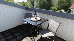 Un pequeño balcón exterior con una mesa, una silla, una botella de vino y una copa.