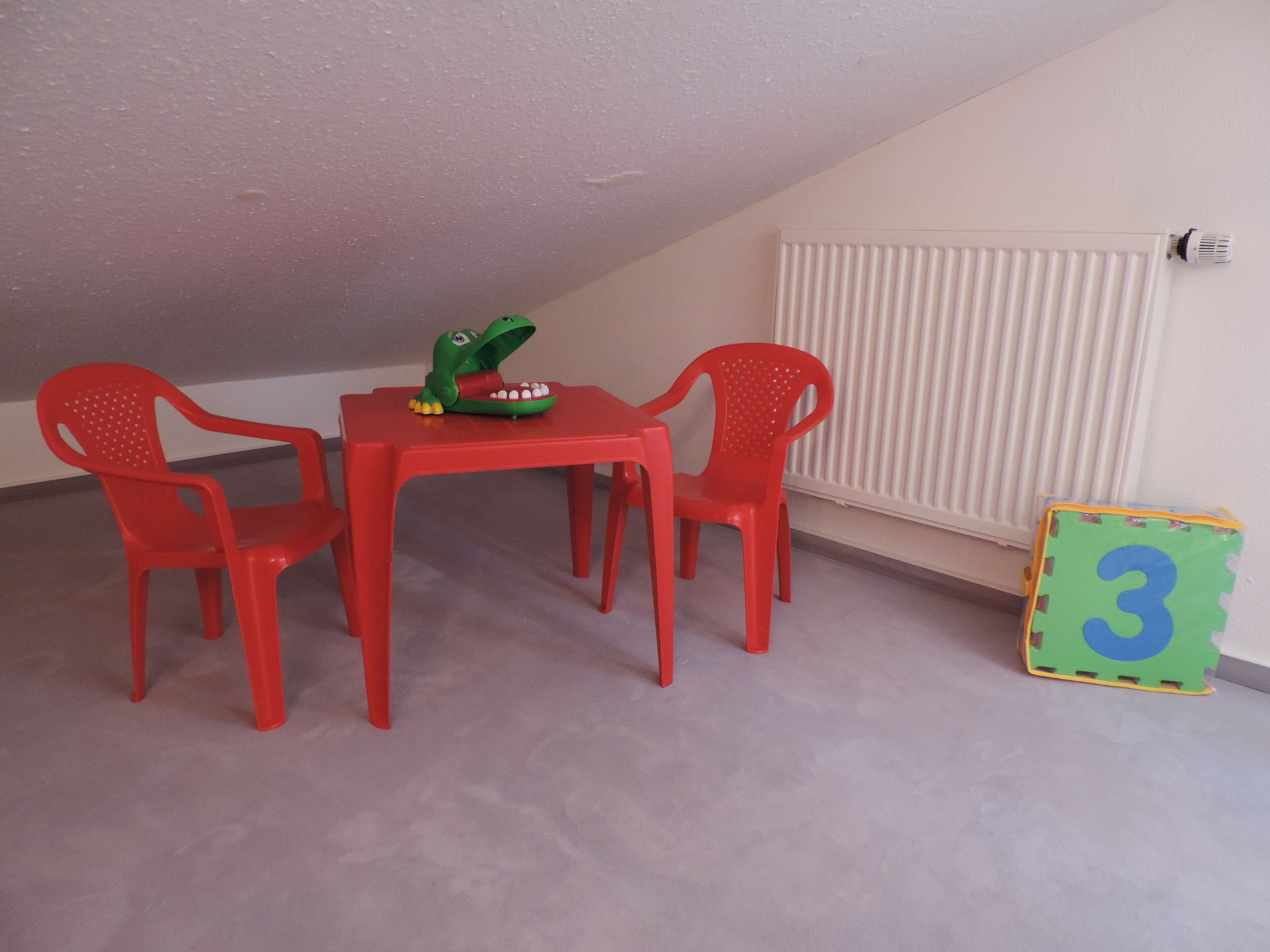 Ein Zimmer mit einem roten Tisch und Stühlen, einem grünen Spielzeug und einem Bauklotz mit der Zahl 3.