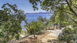 Un sentier en bois mène à un belvédère offrant une vue panoramique sur la mer et les montagnes lointaines.