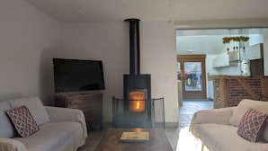Ein Wohnzimmer mit Kamin, Sofas, einem Fernseher und einer durch eine offene Tür einsehbarer Küche.
