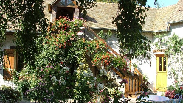 Ein rustikales Haus mit einer Holztreppe, einer kleinen Veranda und einem Garten mit blühenden Pflanzen.