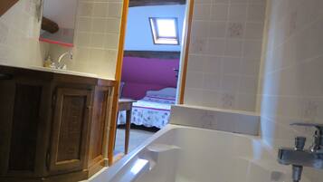 Une salle de bain avec une baignoire, un lavabo et un miroir. Il y a une fenêtre au-dessus du lavabo et une porte qui donne sur une autre pièce.