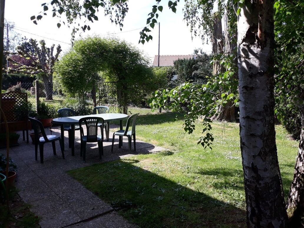 Une terrasse avec une table et des chaises, entourée d’arbres et d’une clôture.