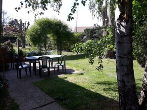 Un patio con mesa y sillas, rodeado de árboles y una valla.