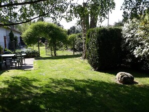 Un jardín con una mesa y sillas, un árbol grande y un seto.