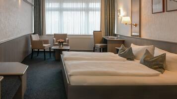 A hotel room with a large bed, two armchairs, a small table with a vase of flowers, and a desk.