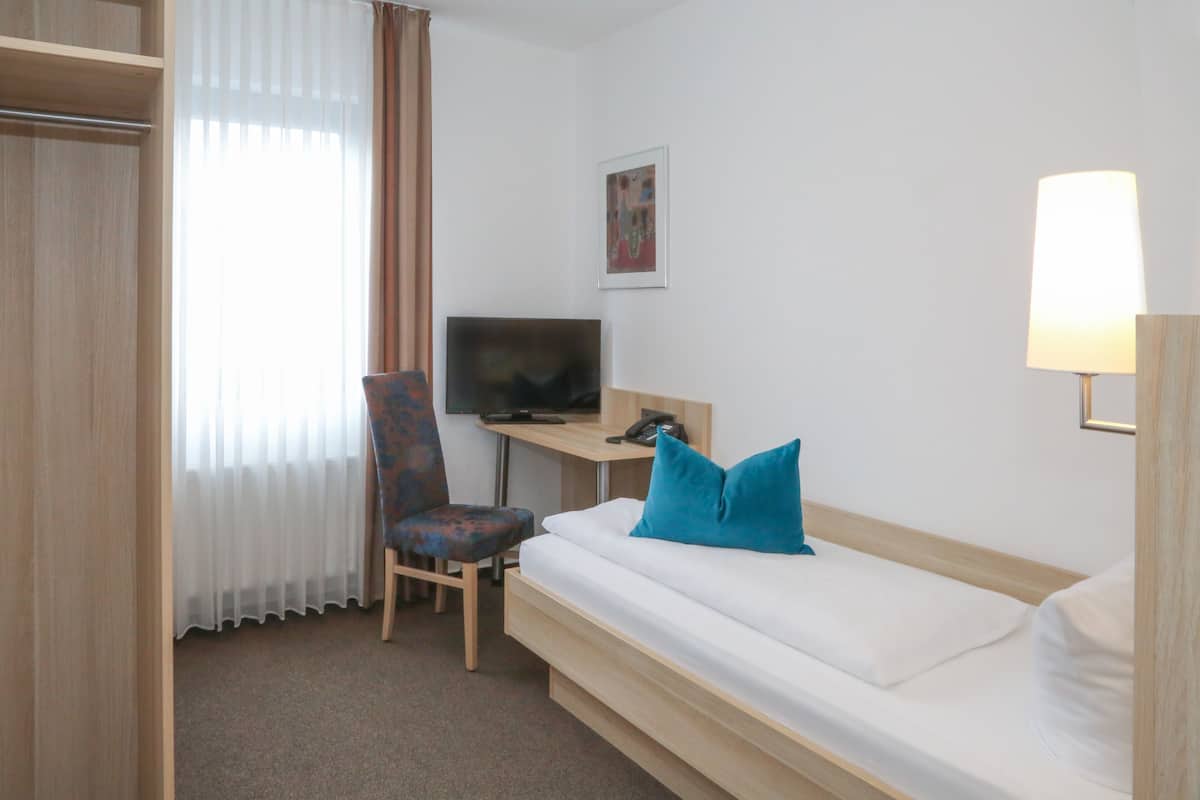 A hotel room with a bed, a desk with a computer, a chair, and a television.