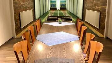 A conference room with a long table, chairs, a projector screen, and a brick wall.