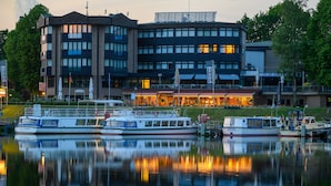 A waterfront hotel with multiple decks and a reflection in the water. - Hotel am Wasserfall (Lingen)