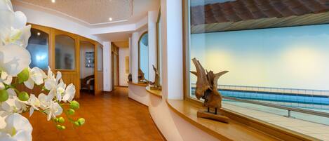 A hotel corridor with a view of a pool through large windows.