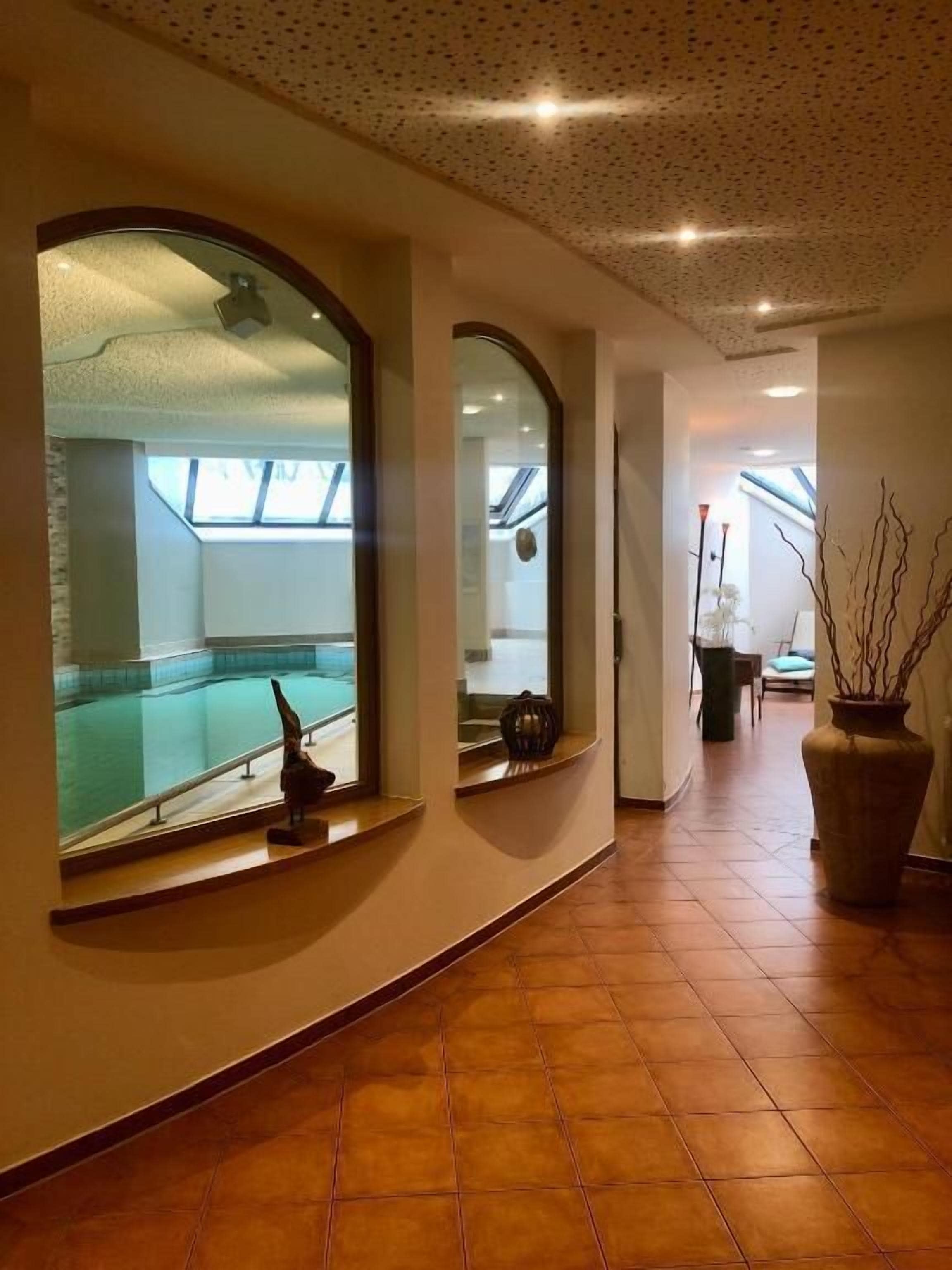 A corridor with a large arched window, a potted plant, and a tiled floor.