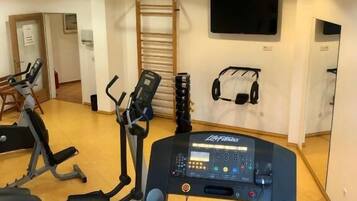 A gym with cardio equipment, a wall-mounted TV, and a mirror.