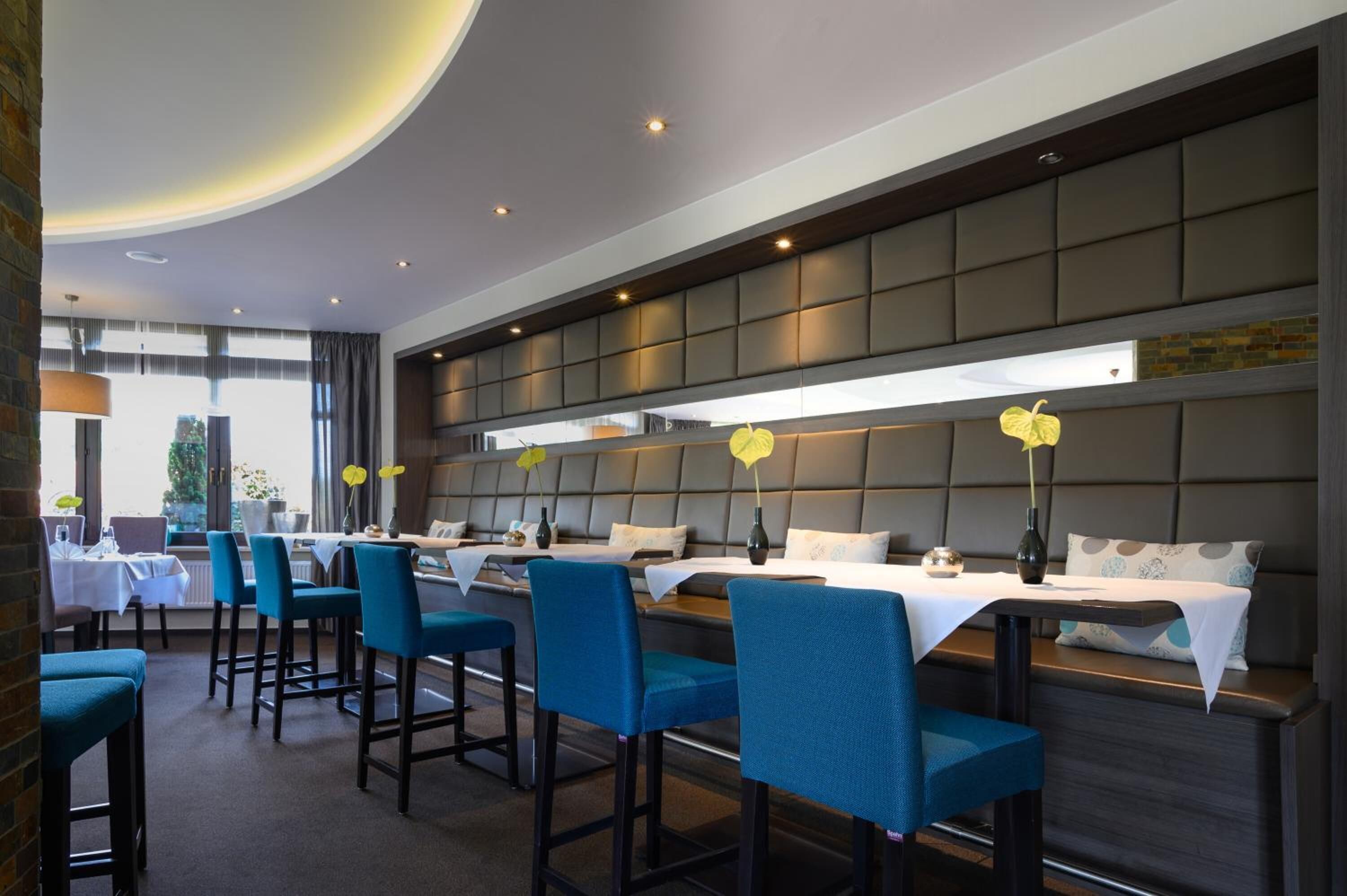 A modern restaurant with a long counter and blue upholstered chairs.