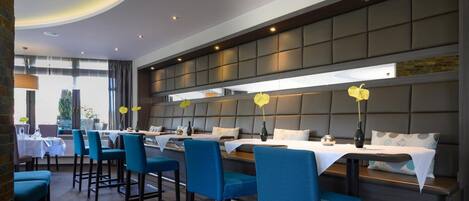 A modern restaurant with a long counter and blue upholstered chairs.