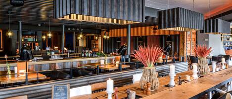 Un restaurant moderne avec des tables en bois, des luminaires suspendus et un espace bar.