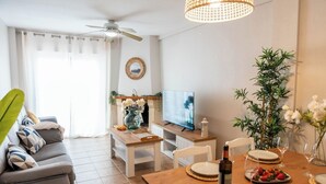 A living room with a sofa, TV, dining table, and a ceiling fan.