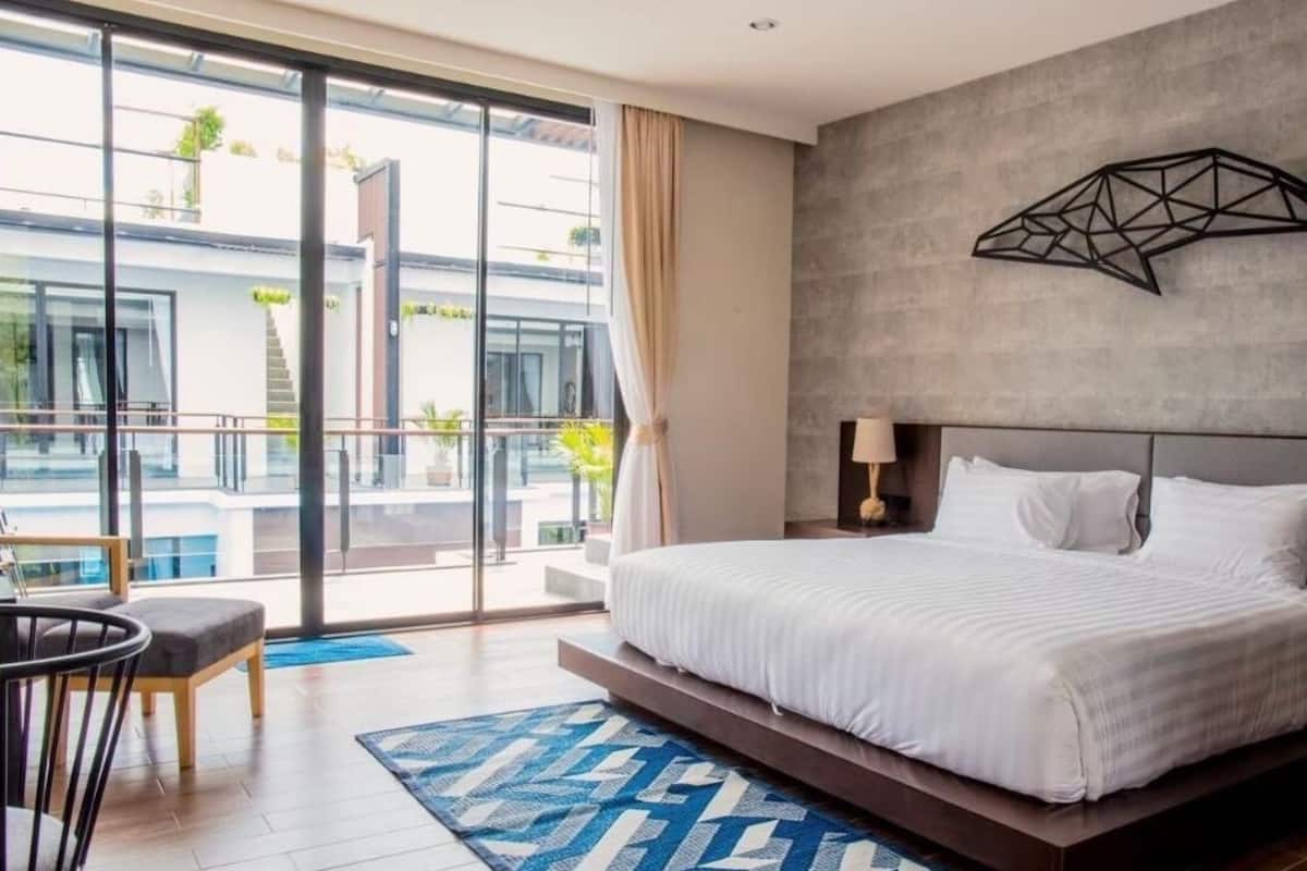 Une chambre d’hôtel moderne avec un grand lit, une vue sur la piscine et une œuvre d’art géométrique accrochée au mur.