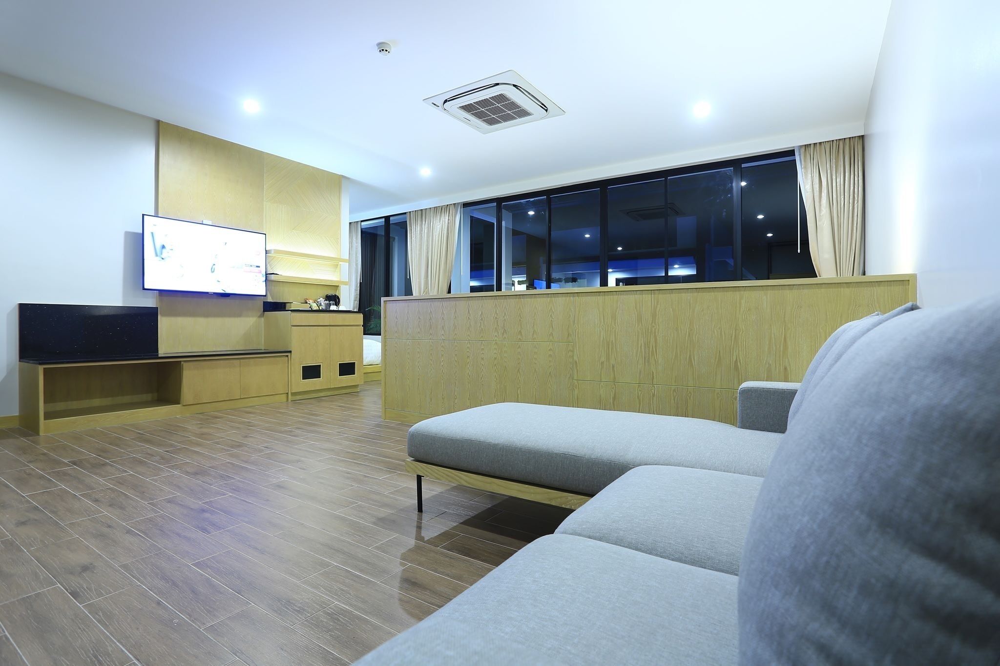 Habitació d'hotel moderna amb un sofà, una televisió, un armari de fusta i una finestra amb cortines.