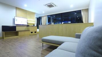Habitació d'hotel moderna amb un sofà, una televisió, un armari de fusta i una finestra amb cortines.