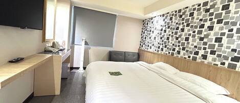 A hotel room with a bed, a desk, a flat-screen TV, and a wall with a mosaic pattern.