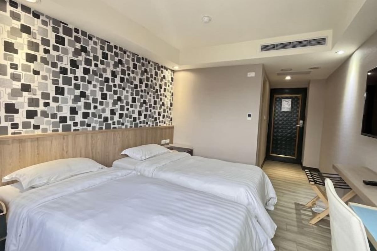 A hotel room with two beds, a TV, and a modern wall design.