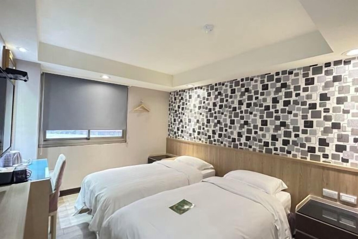 Habitación de hotel con dos camas individuales, un escritorio con silla, una mesita de noche pequeña y una pared con diseño de mosaico.