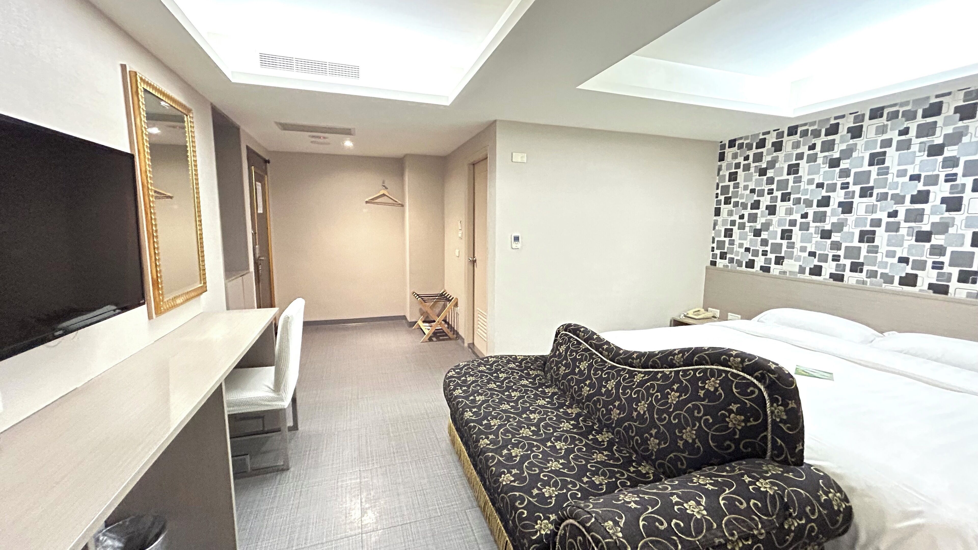 Ein modernes Hotelzimmer mit einem großen Bett, einer Couch, einem Fernseher und einem Spiegel.