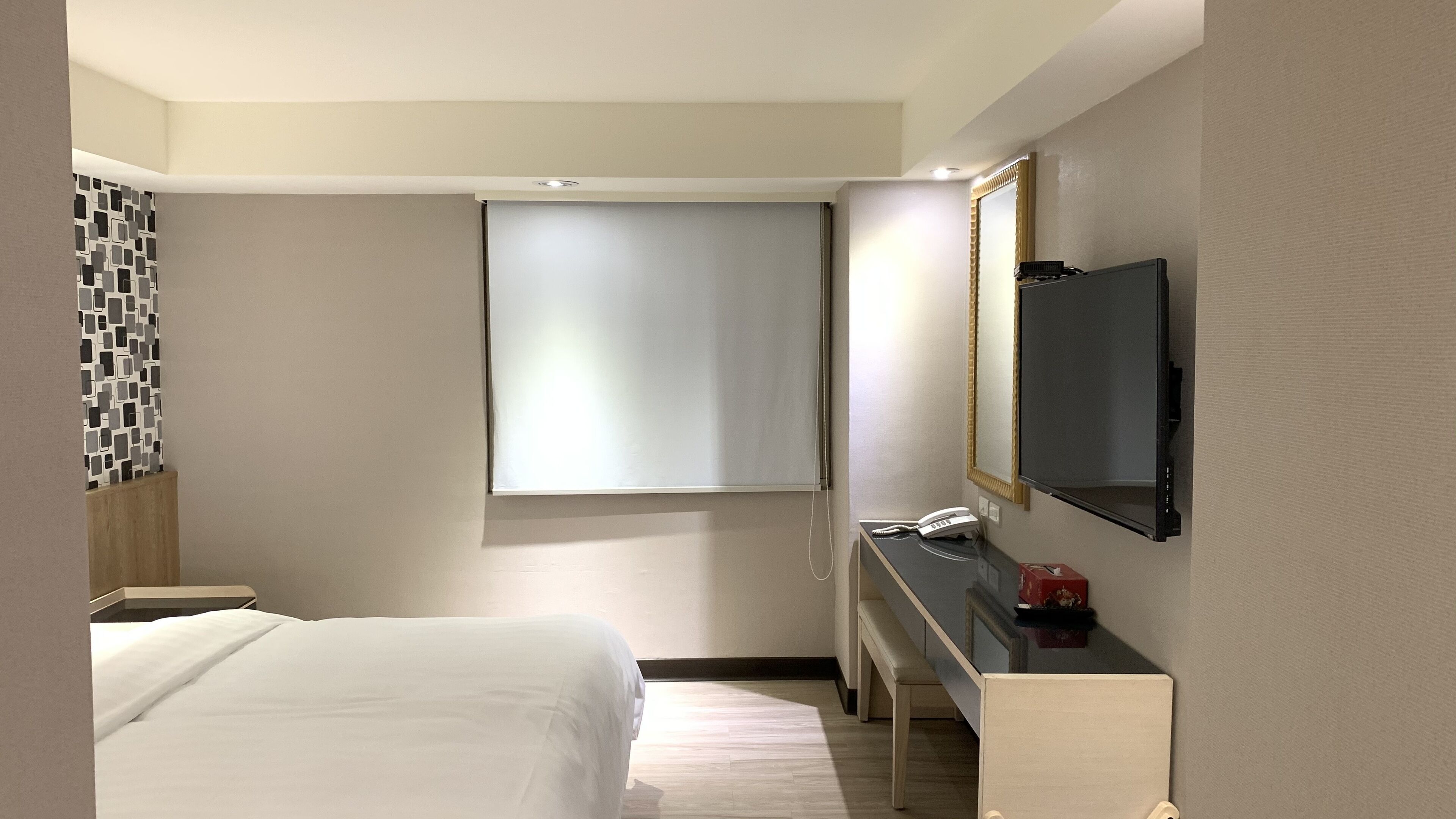Una habitación de hotel con cama, escritorio, espejo, televisión y ventana.