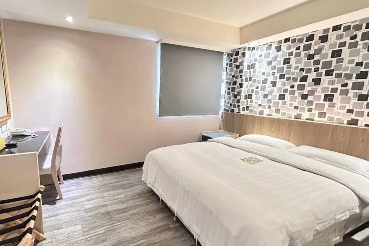 A hotel room with a bed, a desk, a chair, a TV, and a wall with a mosaic pattern.