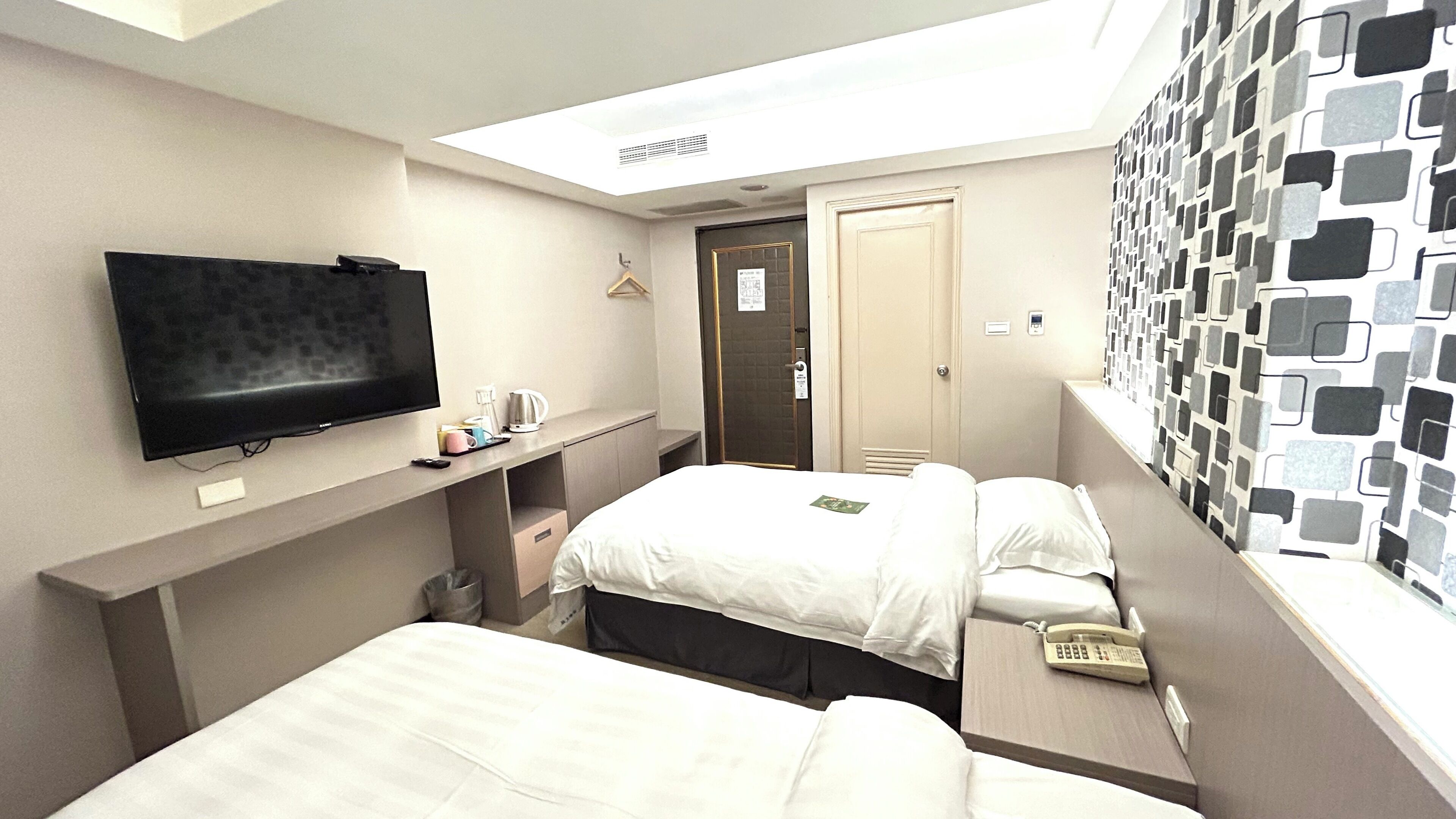Quarto de hotel com duas camas, uma TV de tela plana, telefone ao lado da cama e janela com vista estampada.