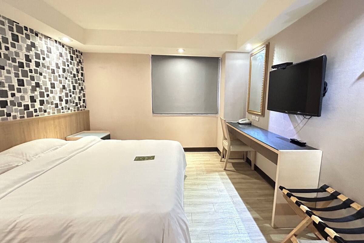A hotel room with a bed, a desk, a chair, a TV, and a wall with a mosaic pattern.