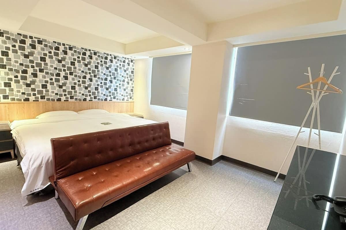 A modern hotel room with a bed, a bench, a desk, and a large window.