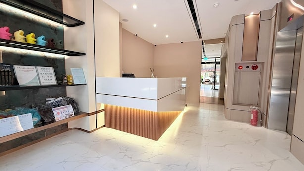 A modern reception area with a white counter, wooden paneling, and a glass display shelf. - Jinhwa Hotel (Keelung)