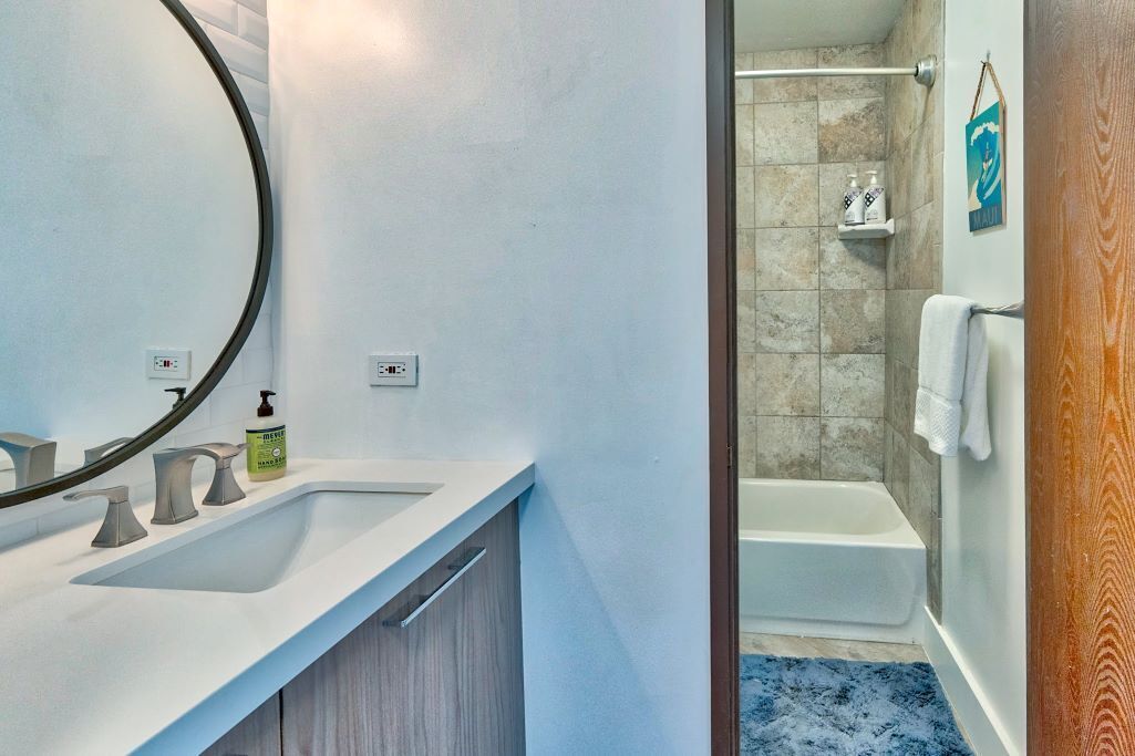 A modern bathroom with a white sink, a large mirror, and a shower area.
