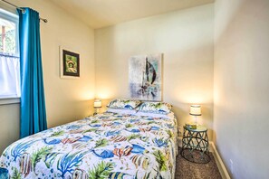 A bedroom with a bed, two bedside lamps, a small table, and a painting on the wall. - Oceanfront Cottage w/Deck & Secluded Beach Access! (Yachats)