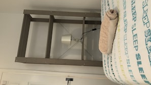 A room with a metal ladder structure, a ceiling light fixture, and a rolled-up towel on a bed with a pillow with 'SLEEP' printed on it. - 2 bedroom Apartment  Heathrow Airport (Hayes)