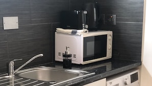 A compact kitchen with a sink, a microwave, a coffee maker, and a washing machine. - 2 bedroom Apartment  Heathrow Airport (Hayes)