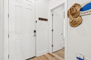 Un pasillo con puertas dobles blancas, un perchero con sombreros y un cartel en la pared.