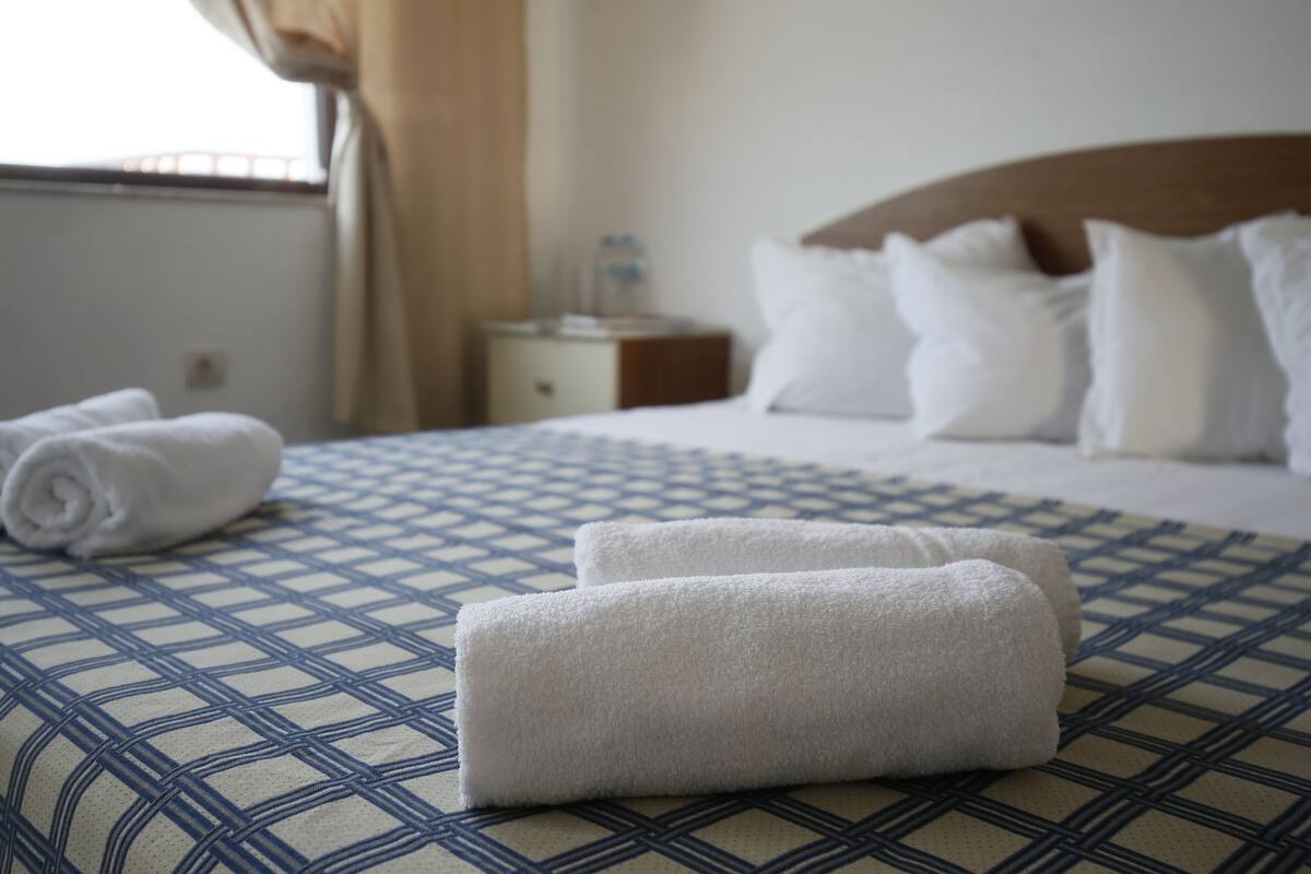 Una cama bien tendida con sábanas blancas y una colcha azul estampada.