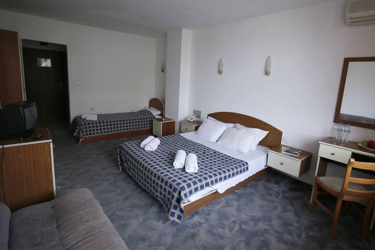 Habitación de hotel con dos camas individuales, un escritorio de madera, una silla, un televisor y un espejo.